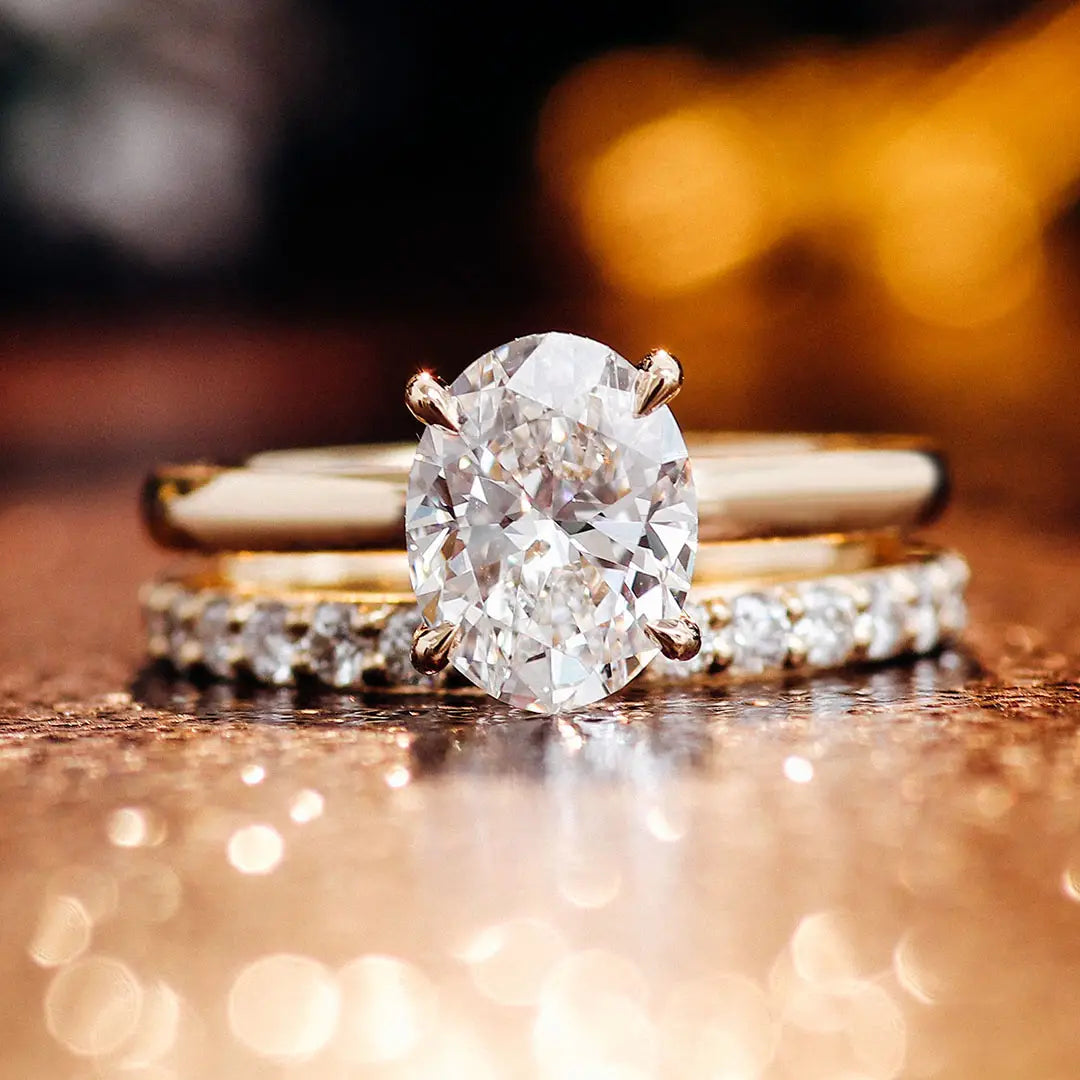Ensemble de bague de fiançailles en diamant de laboratoire ovale, or, présentant une bague à diamant ovale éclatant dans un bracelet en or épuré, avec deux alliances assorties, l’une unie et l’autre sertie pavée, ornées de diamants plus petits.
