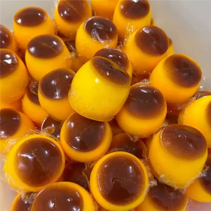 Bonbons gélifiés au caramel brillant jaune vif, avec un cœur translucide brun foncé, conçus comme un jouet sensoriel de type balle anti-stress en forme d’arachide.