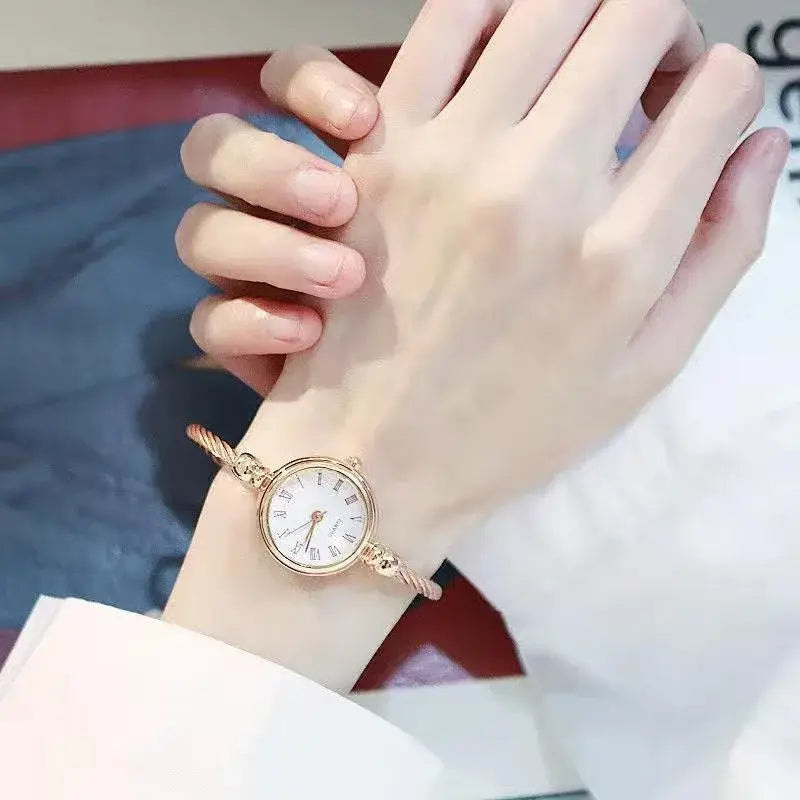 A delicate rose gold-toned women stainless steel quartz bangle watch with a white dial featuring roman numerals and an elegant twisted bracelet design.