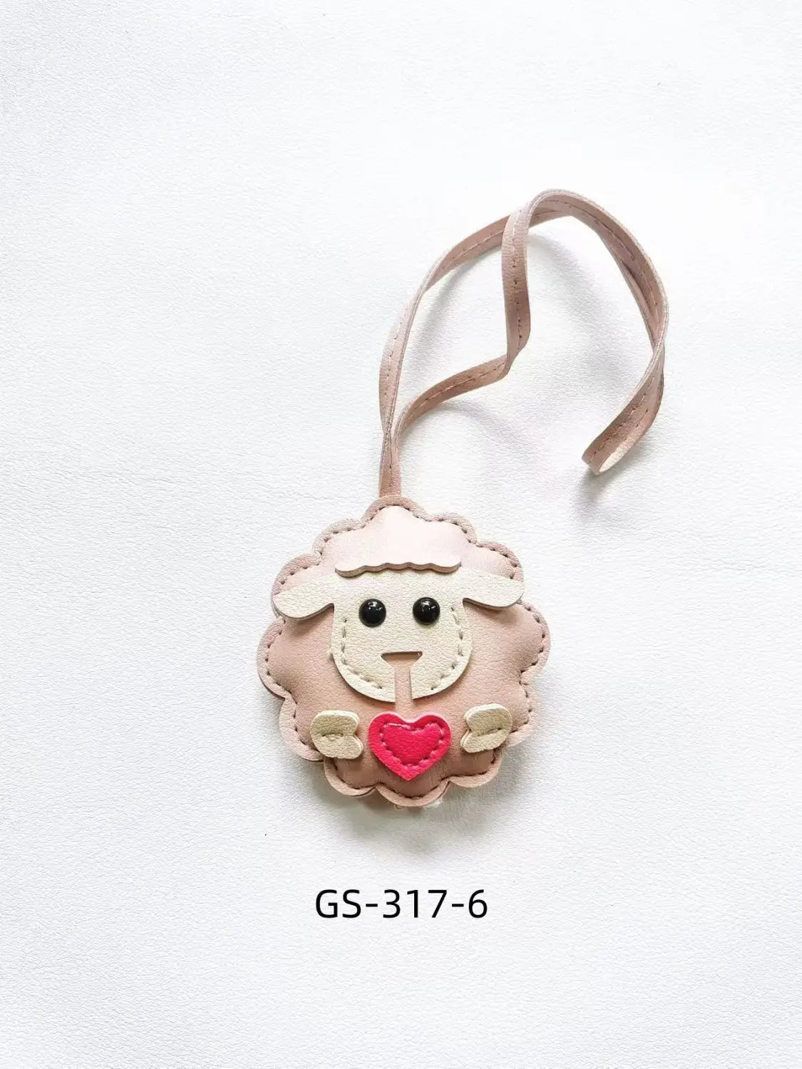 A soft pink leather sheep keychain with black button eyes and a red heart charm attached to a matching ribbon for use as a cute animal bag charm.