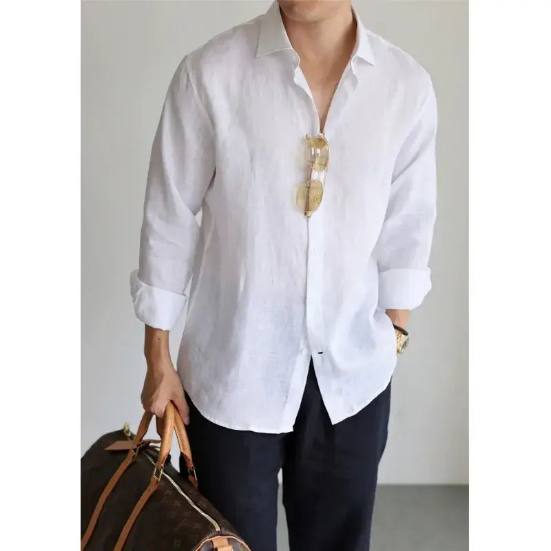 White linen men cotton linen casual button down shirt with rolled-up sleeves and gold-framed sunglasses hanging from the collar.