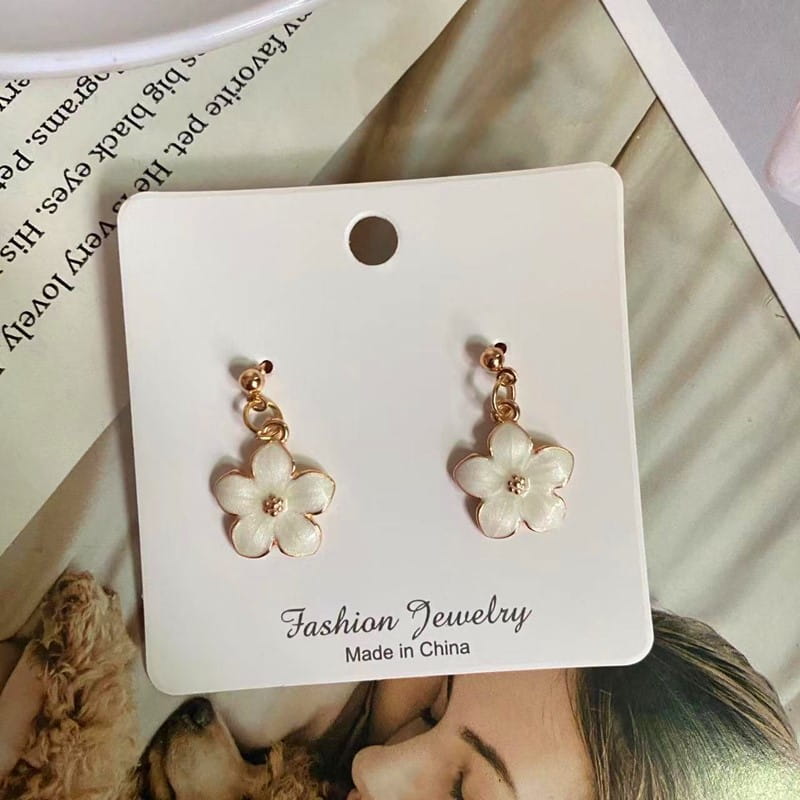 Boucles d’oreilles délicates en fleur émaillée blanche, avec des accents en métal à l’aspect doré et un petit centre en cristal, présentées sur une carte de bijoux de mode ; complètent un collier pendentif de fleur romantique et mignon avec une chaîne à maillons.