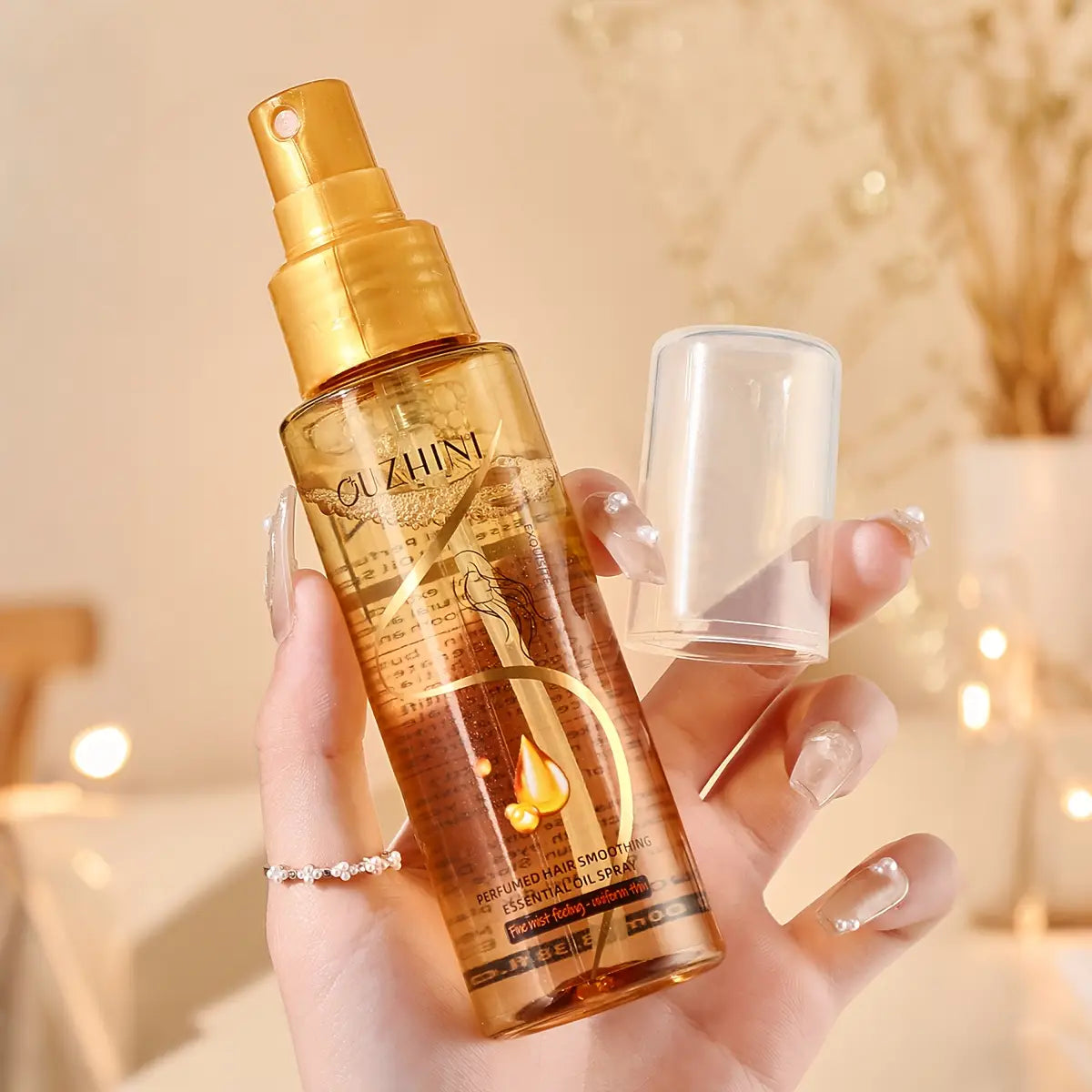 botella dorada con pulverizador del spray esencial de aceite para el cuidado del cabello Quzhini, 100 ml, con tapa transparente y líquido ámbar en el interior, diseñada para uso esencial en el cuidado del cabello.