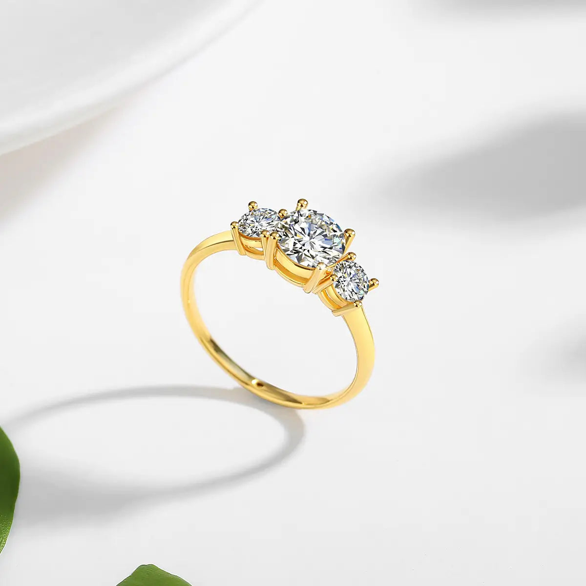 Une bague trois pierres en or 18 carats en moissanite avec une moissanite centrale taillée en rond, flanquée de deux pierres plus petites taillées en rond.