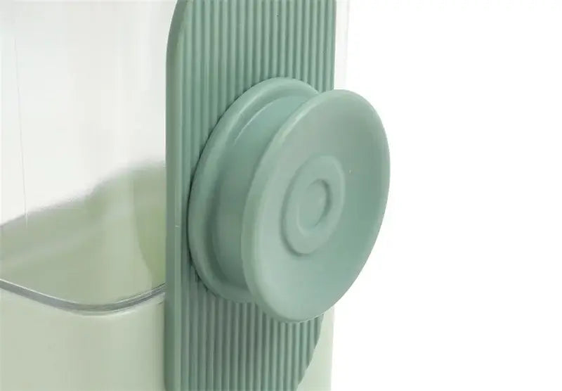 a matte sage green wall-mounted automatic pet feeder made of high-quality plastic featuring a ribbed side panel and circular push-button top for efficient food storage