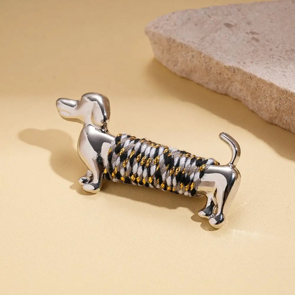 broche en teckel argentée, broche à revers animalière dorée, présentant un design de porte-clés, avec un corps enveloppé d’une corde tressée noire, blanche et dorée.