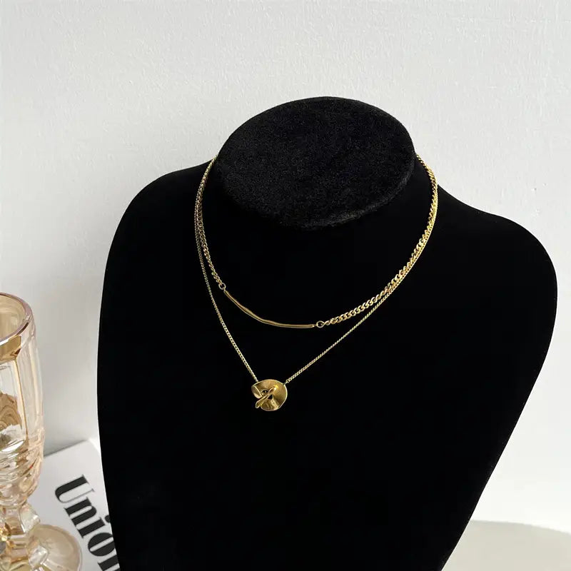 Collier pendentif à superposition géométrique doré pour femmes, présentant une chaînette délicate aux tons dorés avec un petit pendentif en forme de feuille finement détaillé.