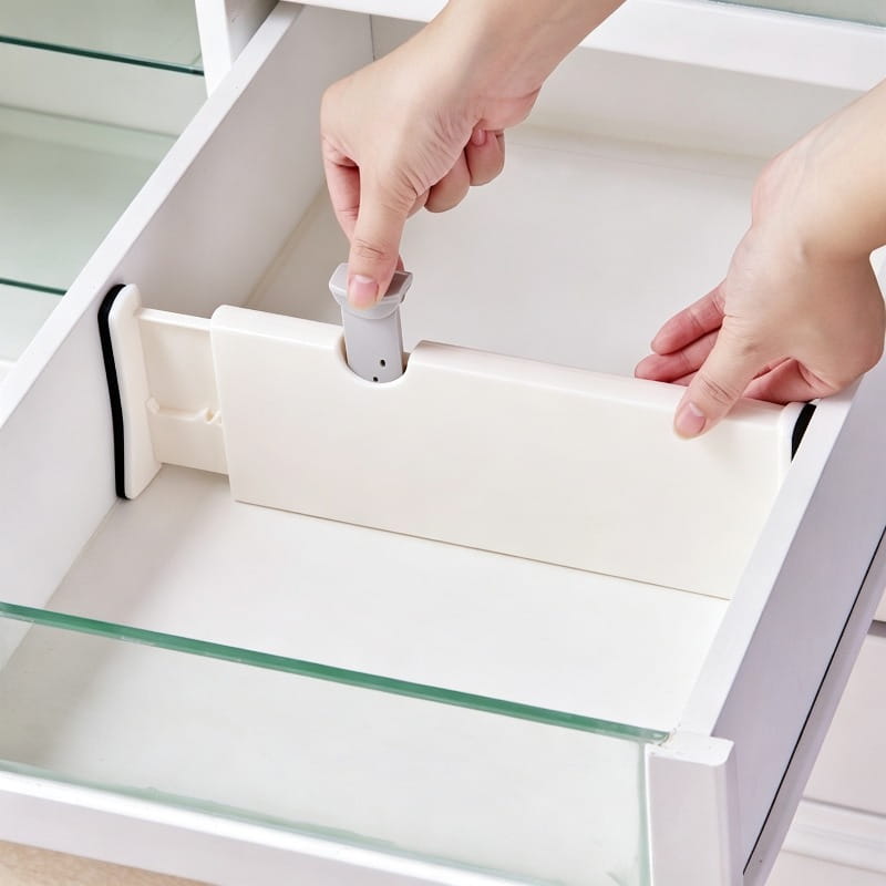 cloison de tiroir en plastique blanc avec un bouton de réglage gris et des bandes en caoutchouc noir pour un ajustement sûr dans une séparation de rangement en plastique ajustable.
