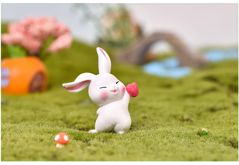 Une figurine miniature en résine céramique blanche de lapin, avec des oreilles internes et des joues roses, tenant un petit cœur rouge pour la décoration d’un jardin féerique.
