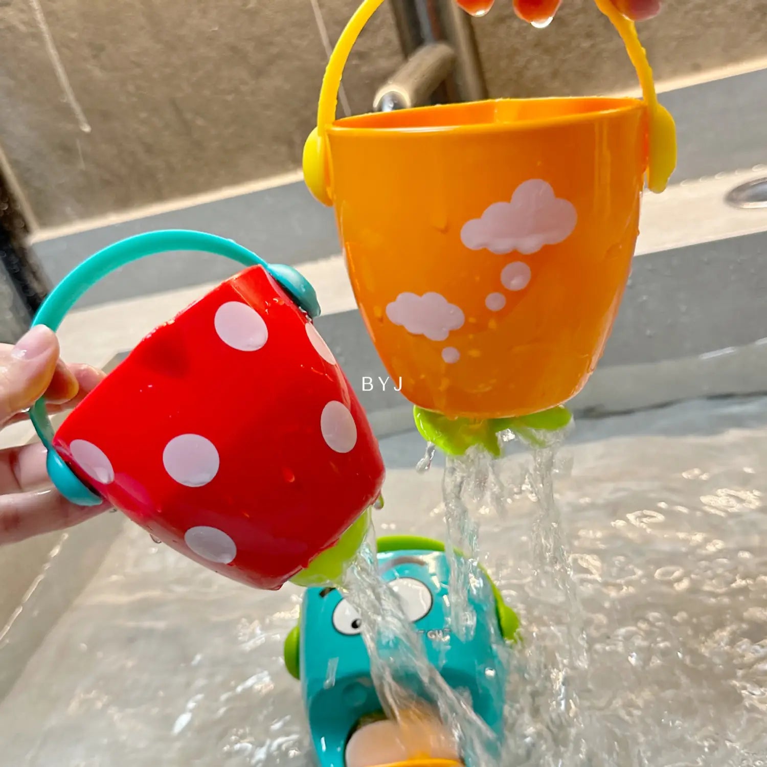 Spielset für Baby-Badewannen-Eimer mit Wassersprühfunktion, bestehend aus orangefarbenen und roten Kunststoff-Eimern mit Griffen; einer ist mit weißen Punkten verziert, der andere mit rosa Wolkenmustern.
