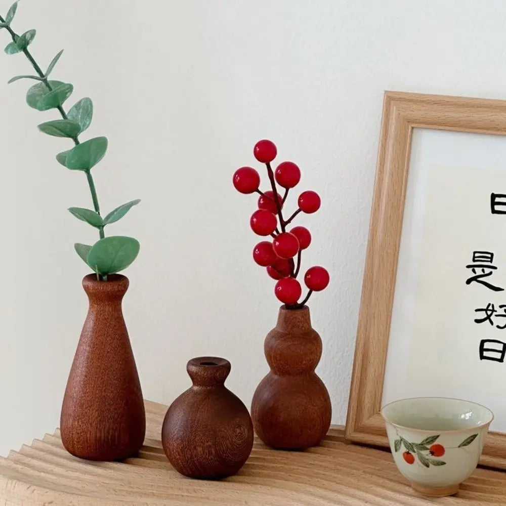 Three rustic brown wooden flower vases of varying shapes with a minimalist design holding decorative foliage for tabletop decor.