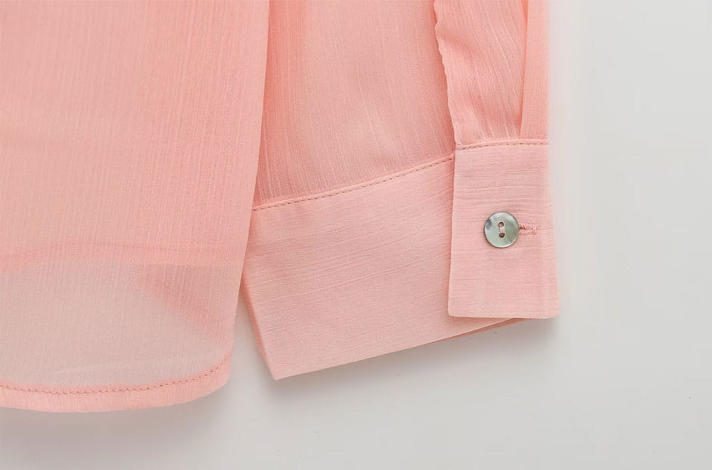 A soft pink textured ruffled button up blouse featuring a lightweight cotton cuff with a subtle weave and a small silver button.