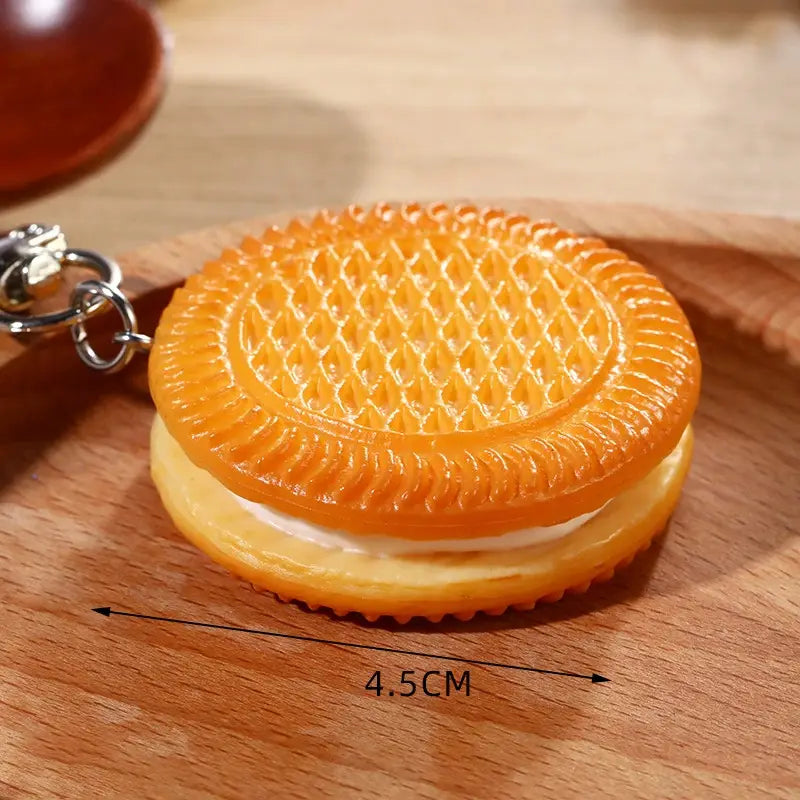 Orange-colored glossy plastic keychain shaped like a miniature chocolate biscuit cartoon with detailed grid patterns on the top and bottom halves, used as a bag pendant.