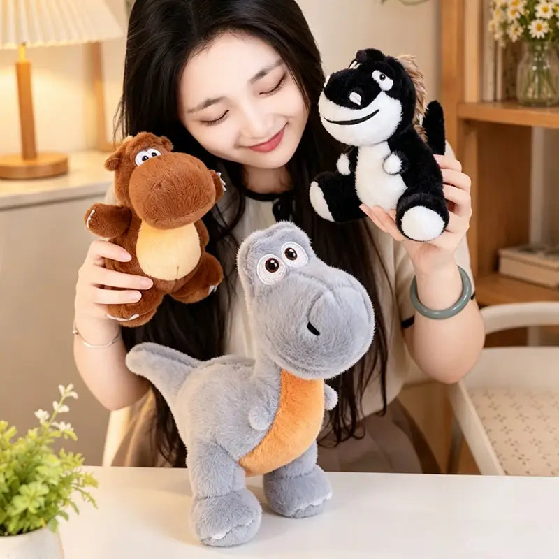 Dinosaure en peluche gris avec un ventre orange et des yeux cousus, debout sur une table : une peluche de dinosaure colorée fabriquée en matériau de peluche souple.