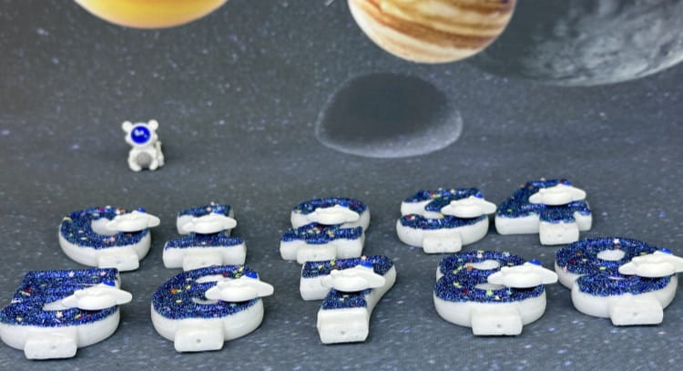 Velas con números azules y blancas con brillo y temática espacial, con diseños de nubes, utilizadas como adornos para pastel de fiesta planetaria.