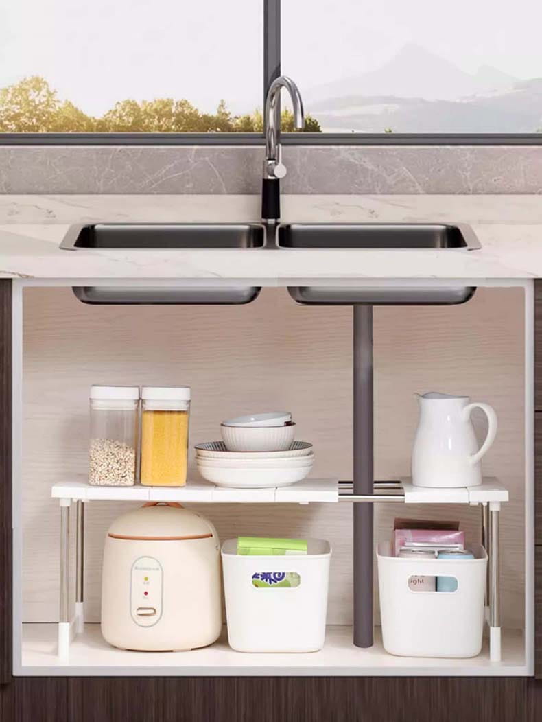 Étagère sous évier blanche avec pieds métalliques réglables et barre centrale, conçue comme un support télescopique pour évier et une étagère de séparation à couches pour l’organisation de la cuisine.