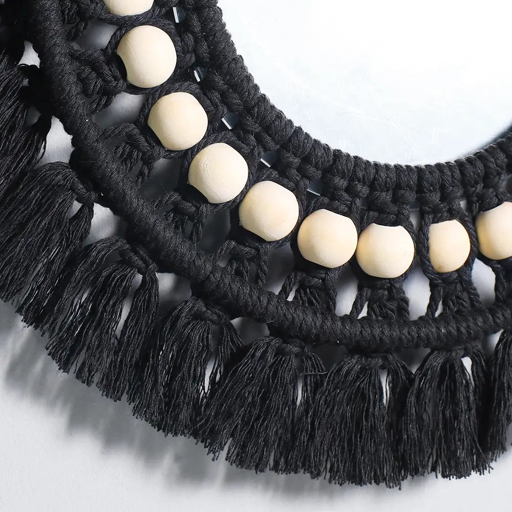 black macrame necklace with cream-colored wooden beads and fringe displayed alongside a round macrame wall mirror boho decorative mirror designed as a decorative wall mirror.