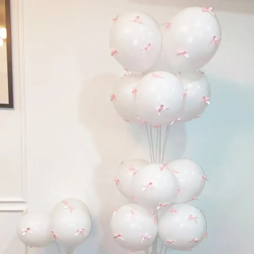 Un assemblage de ballons blancs avec de délicats nœuds en ruban rose, conçu pour la décoration de fête dans un ensemble de ballons à nœud blanc.