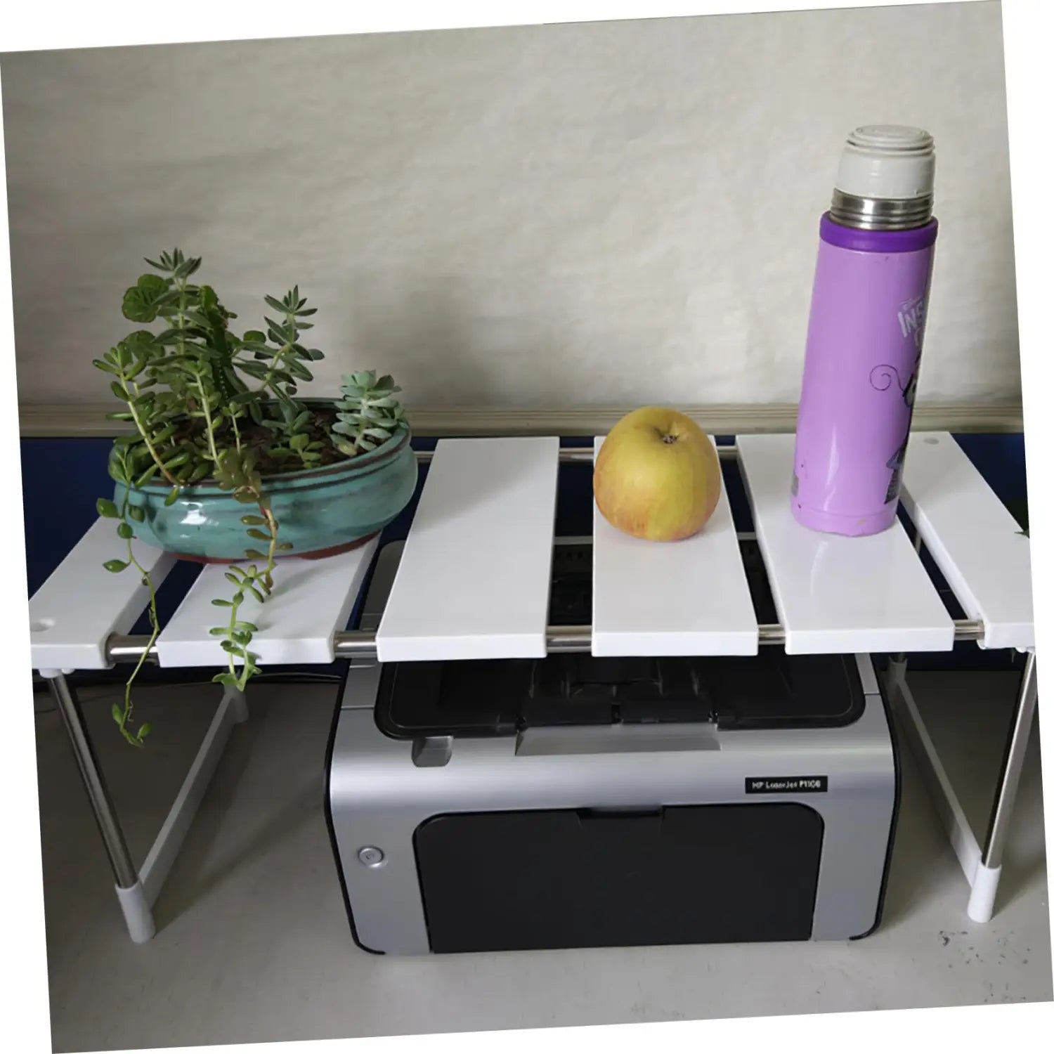Une thermos isotherme isolé pourpre avec un couvercle argenté et un motif décoratif de lettrage affiché sur un comptoir de cuisine blanc, sur une étagère-organisateur de rangement.