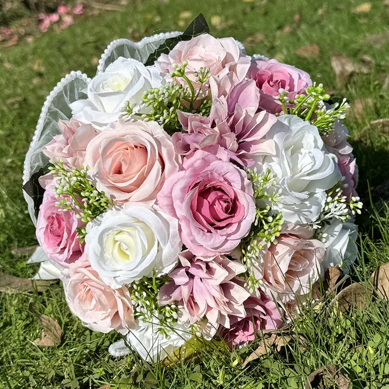 A delicate white silk rose wedding bouquet with lace and pearls featuring artificial roses and dahlias in soft pink blush and white hues wrapped with a sheer lace ribbon.