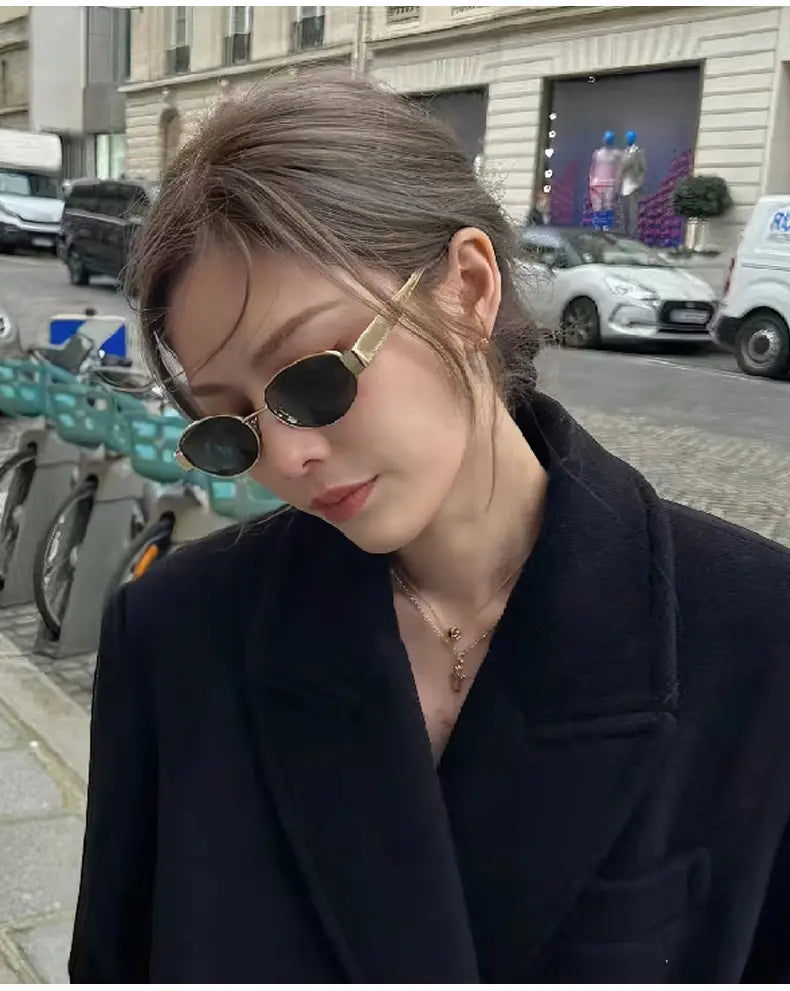 Una mujer que lleva gafas de sol ovaladas con borde dorado, con lentes oscuras, y una montura dorada para mujer y hombre.