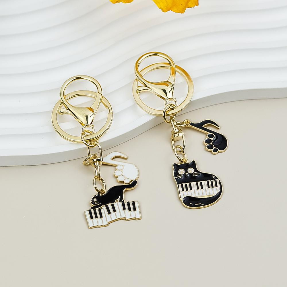 Gold-toned black cat piano keychains with white and black enamel designs featuring a piano keyboard and musical note accented by gold-colored metal clasps perfect for music lovers.