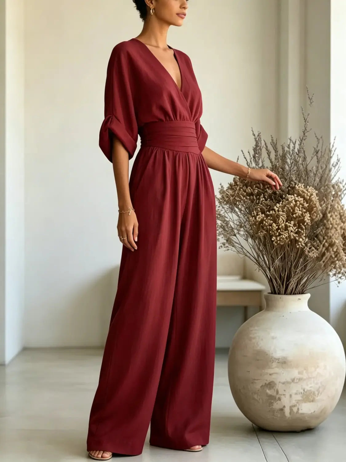 A flowing burgundy v-neck wide-leg jumpsuit with three-quarter sleeves gathered at the cuffs and a cinched waistband.