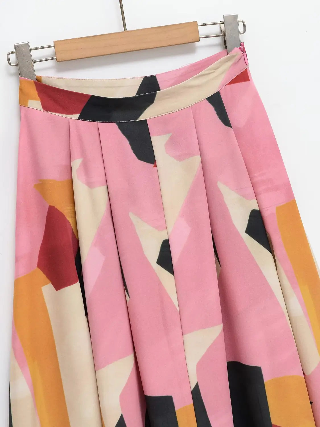 Ein plissierter geometrischer Satin-Midirock mit einem lebhaften abstrakten Muster in Rosa, Orange, Schwarz und Beige.