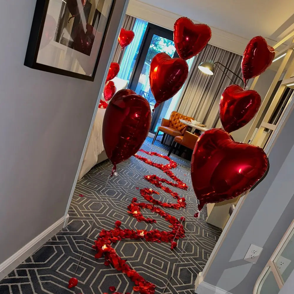 Shiny red heart-shaped balloons and red rose petals arranged along a path as an anniversary decoration set.