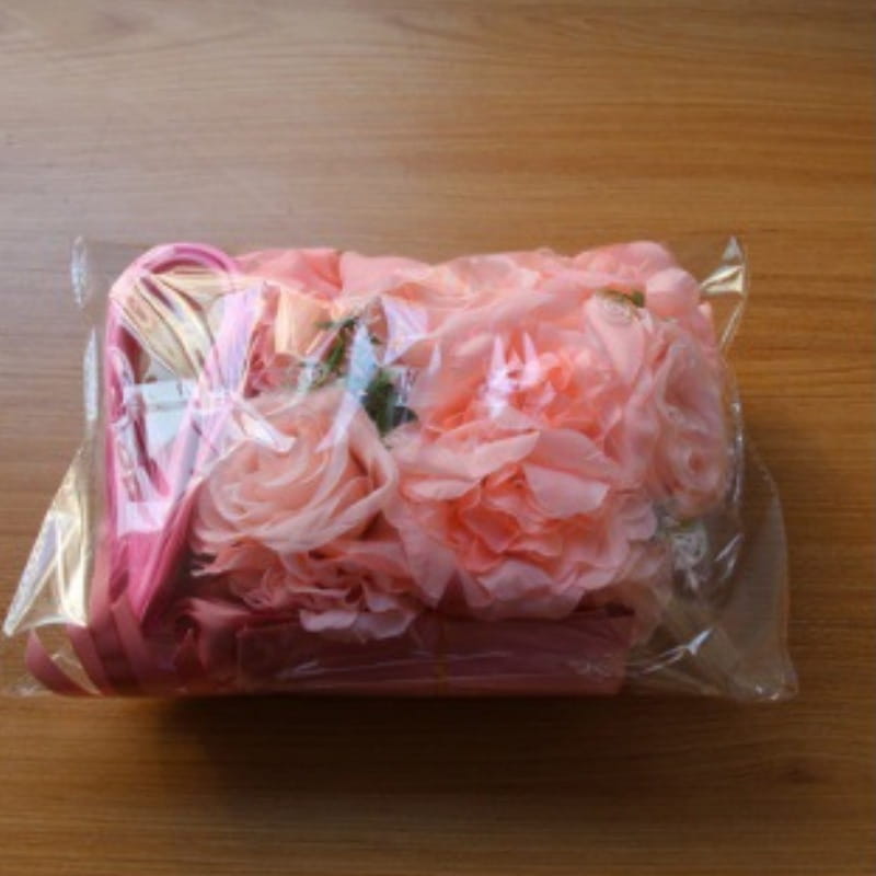 Un sac à main floral rose en tissu froncé en forme de pétales et une poignée à ruban assortie, enveloppés dans un film plastique transparent pour l’ensemble de décoration florale artificielle pour voiture de mariage.