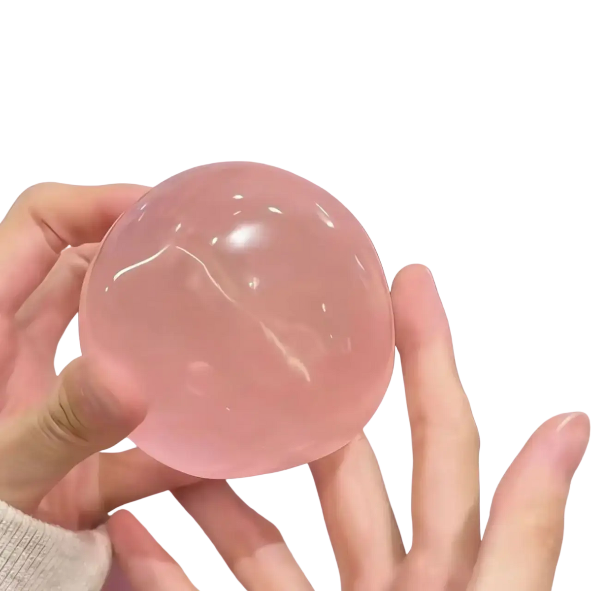 A translucent pink spherical stress ball made of blue coconut oil material held gently in hands for squeezing relief