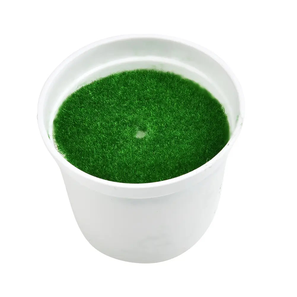 une tasse en plastique blanche remplie de fleurs artificielles vert éclatant, fabriquées à partir d’herbe artificielle, pour la décoration intérieure du domicile, en pot.