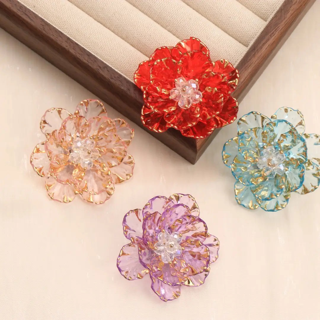 Broche en forme de fleur de cristal, accessoire de mode, présentant des cristaux rouges, roses, bleus et pourpres vibrants, avec des pétales bordés d’or et des centres en pierre précieuse transparents.
