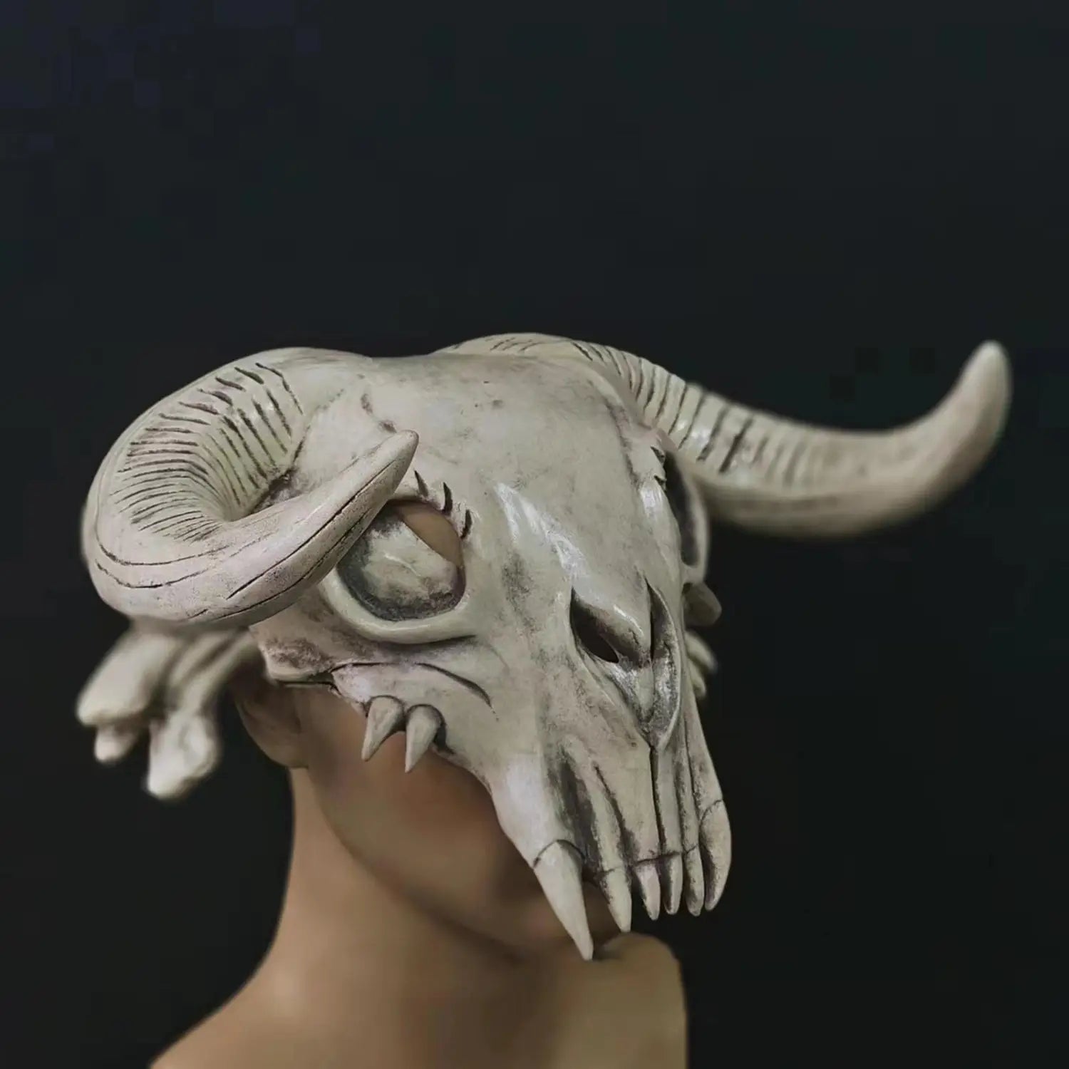 A detailed off-white halloween cosplay mask featuring a horned ram skull with intricate carvings and sharp teeth as a creepy head mask.