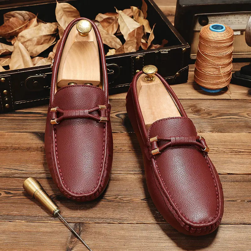 Chaussures à enfiler habillées en cuir bordeaux pour hommes, avec des boucles métalliques ton or et une couture détaillée, conçues pour un port décontracté sans effort.