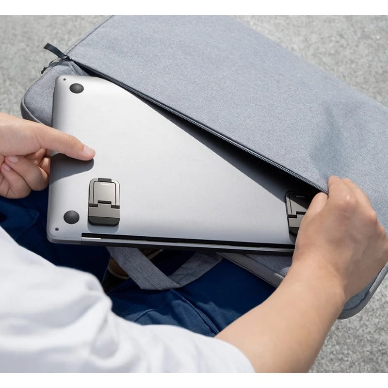 silberner Mini-Aluminium-Laptopständer mit integrierter Stütze und schwarzen runden Anschlüssen, eingebettet in eine graue Stoffhülle für die tragbare Notebook-Nutzung.