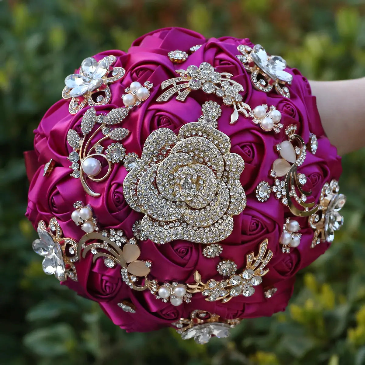 Un bouquet de mariée en satin fuchsia présentant des embellissements en perles serties de strass dorés, ainsi qu’une broche centrale en forme de rose étincelante.