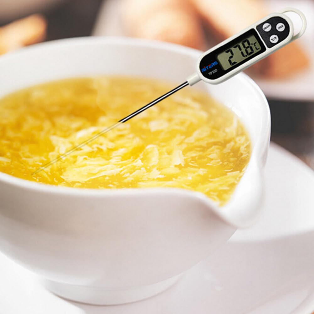 Weiße digitale Fleischthermometer für sofortiges Ablesen mit schwarzem Display und Tasten, eingesetzt in eine Schüssel gelber Eierdrop-Suppe.