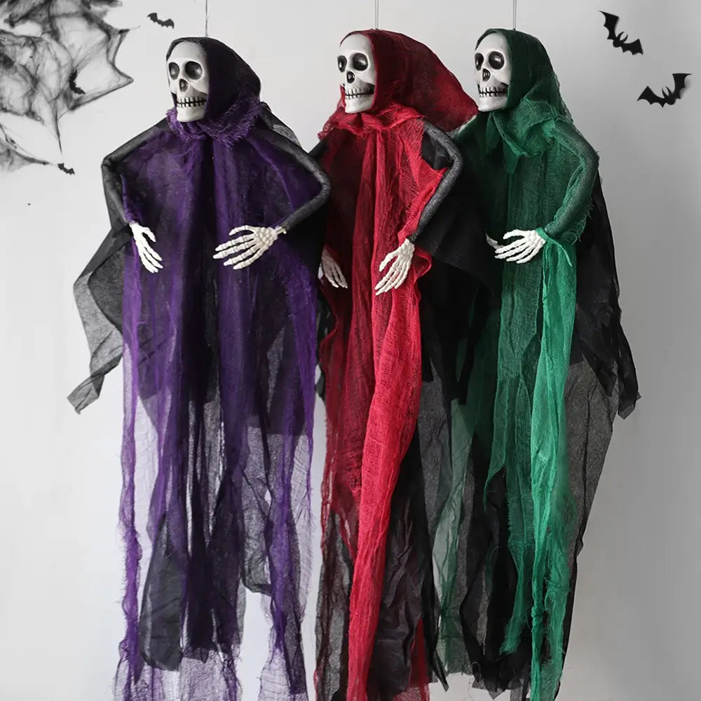 Trois décorations d’Halloween de fantôme squelettique suspendu, drapées dans des manteaux en tissu translucide fluide violet, rouge et vert, avec des couches intérieures noires et des mains squelettiques blanches.