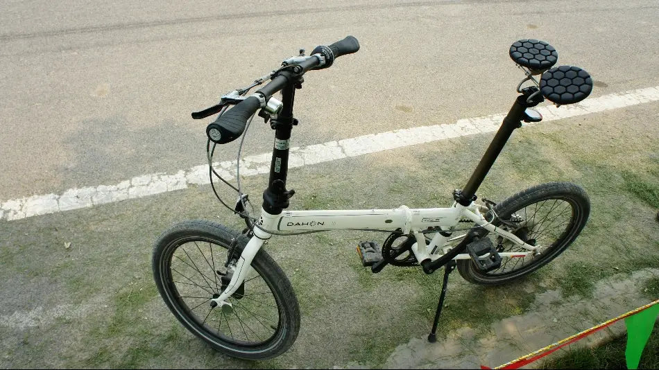 Ein weißes Dahon-Faltrad mit schwarzen Lenkergriffen, Reifen und einem markanten, sechseckig gemusterten nasenlosen ergonomischen Fahrradsattel.