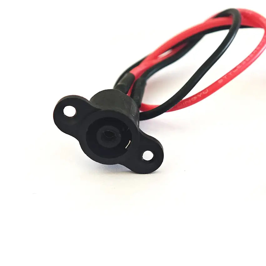 Puerto de carga del patinete Xiaomi M365 de plástico negro con cubierta impermeable y cables rojo y negro mostrados desde la cara posterior.