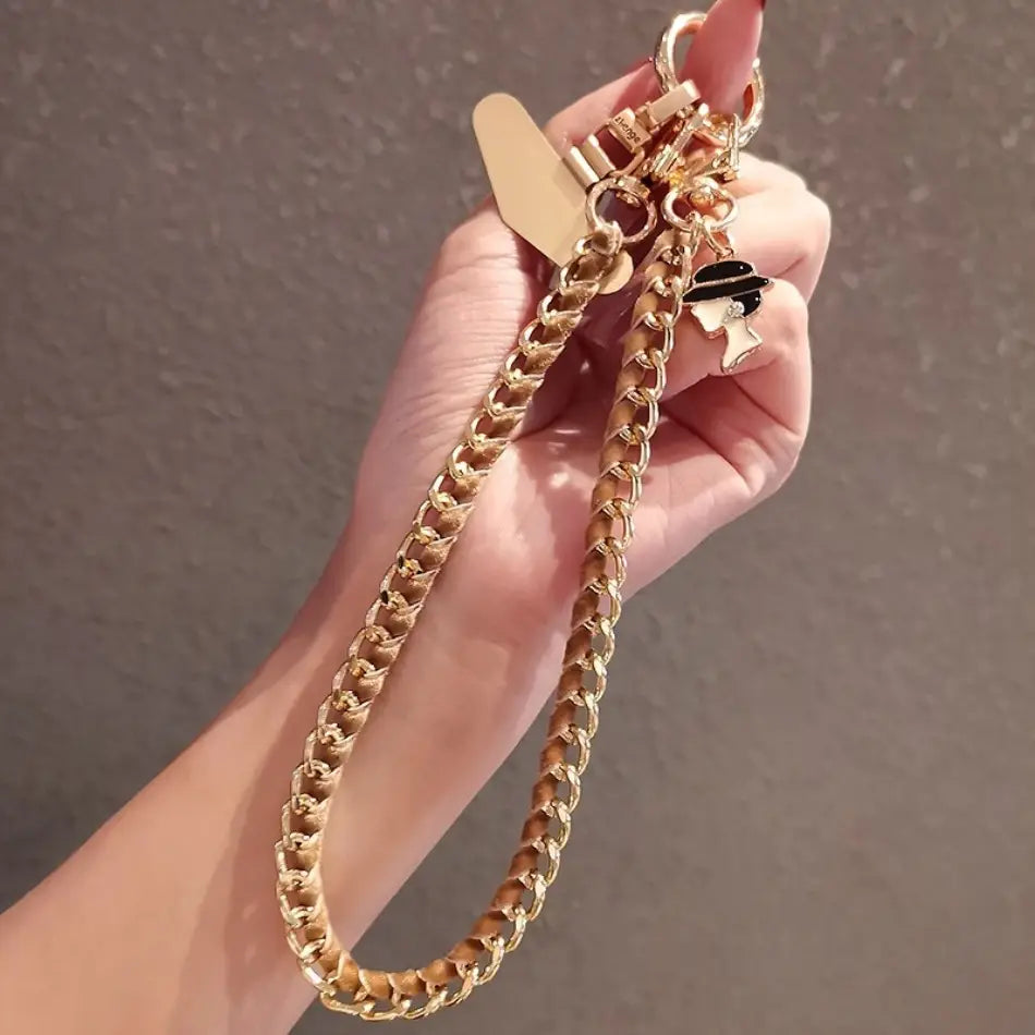 Handy-Handgelenkriemen aus goldfarbener Kette als Anti-Lost-Handylanyard mit einem goldfarbenen Kettenhandtaschenriemen, mit einem herzförmigen Anhänger und einem schwarz-weißen Emaille-Anhänger.