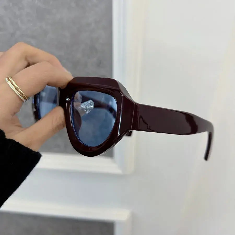 Gafas de sol geométricas burdeos para mujeres y hombres con monturas angulares de acetato brillante color marrón oscuro y lentes con tonalidad azul.