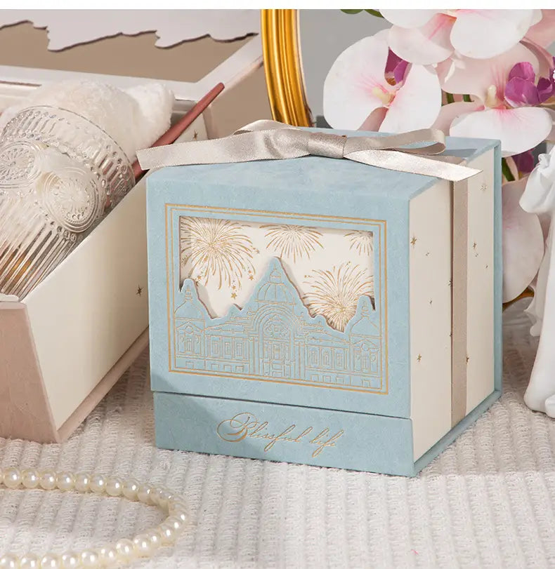 light blue and cream european style wedding gift box candy packaging made of paper with gold foil detailing and a cut-out fireworks design over an architectural silhouette