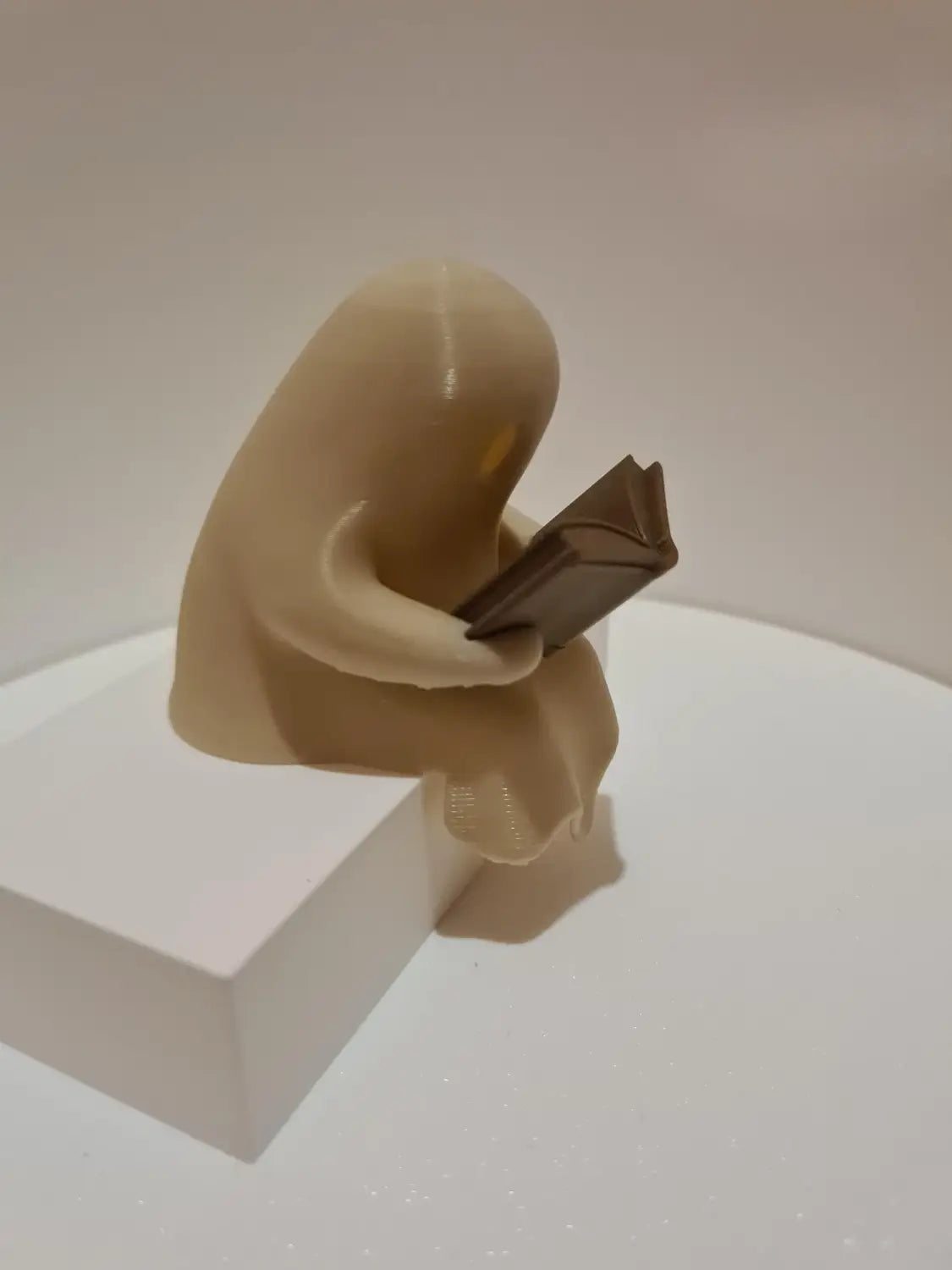 Eine beigefarbene Harz-Geister-Lese-Buch-Figurenskulptur einer sitzenden Gestalt, die ein offenes Buch hält, mit einem flackernden Teelicht.