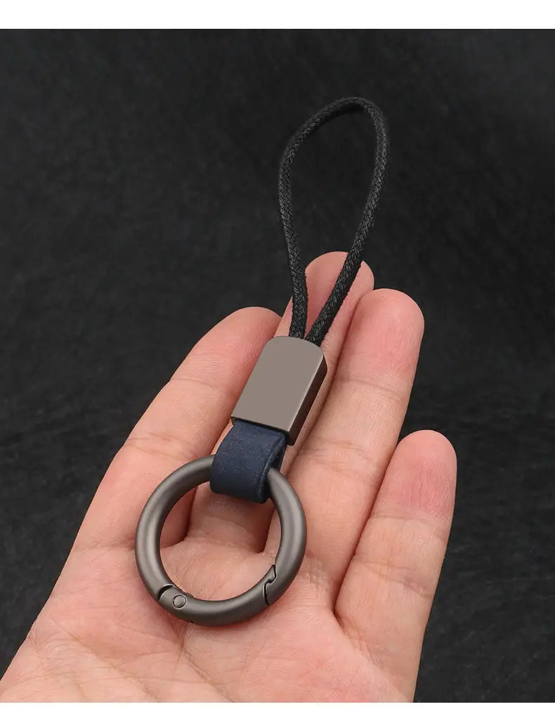 A sleek leather keychain lanyard with a matte-finished metal ring, dark blue leather strap, and black braided cord for car key holding.