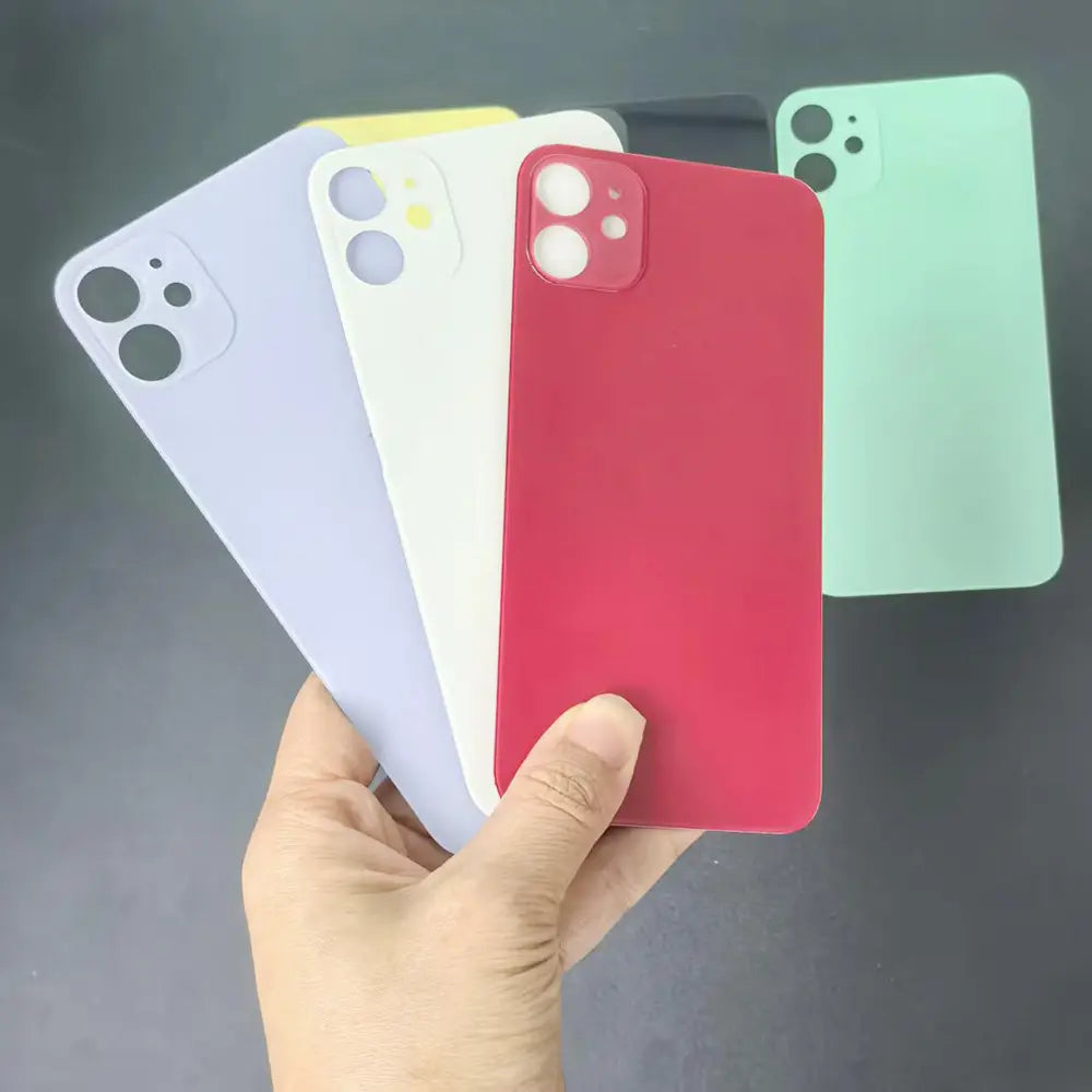 Una mano sostiene una colección de puertas de batería traseras de repuesto para iPhone 11 con acabado mate y lentes de cámara en rojo, blanco, lavanda y verde menta, mostrando el lado posterior del producto.