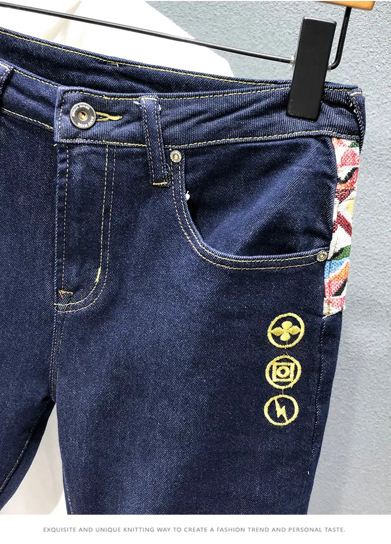 men slim fit stretch white denim jeans in dark blue featuring gold embroidered circular logos and a colorful patterned patch on the side seam