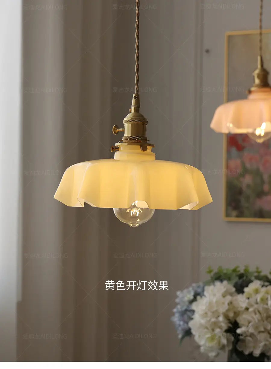 Luminaires suspendus de style vintage avec un abat-jour en verre à jupe florale froncée jaune chaud et une tête de lampe en cuivre visible depuis l’avant.