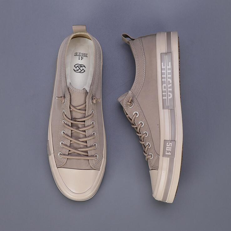 Baskets décontractées en toile beige pour hommes, avec des coques en caoutchouc blanc et des semelles, présentant des rayures latérales grises avec branding urbain conçu comme des chaussures d’été légères.